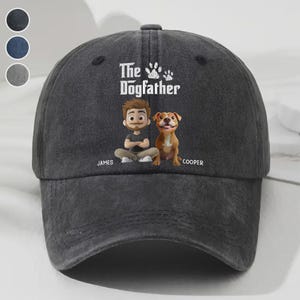 Può includere: Un cappellino da baseball grigio scuro con la scritta "The Dogfather" e un'illustrazione di un uomo e un cane. L'uomo si chiama James e il cane Cooper. Il cappellino ha una visiera curva e un bottone in cima.
