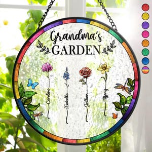 May include: A round stained glass window hanging with a black metal frame. The window has a rainbow border and a white background with the text "Grandma's GARDEN" in black. There are four flowers with names written below them: Caroline, Isabella, Jillian, and Tiffany.