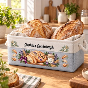 May include: A rectangular fabric storage basket with white rope handles, containing two loaves of sourdough bread. The basket features the text "Sophia's Sourdough" and a graphic of bread, lavender, and a jar labeled "Made with Love".