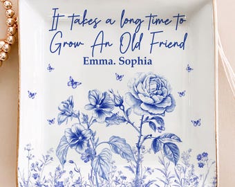 May include: Square white ceramic trinket dish with a gold rim. The dish features a blue floral design with butterflies and the text "It takes a long time to Grow An Old Friend" with the names "Emma. Sophia".