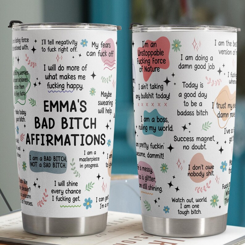 May include: Two stainless steel travel tumblers with black lids. The tumblers are covered in affirmations and phrases like "Emma's Bad Bitch Affirmations" and "I am a badass bitch." The design includes floral and star accents.