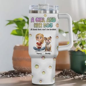 May include: White tumbler with a handle, featuring the text "A GIRL AND HER DOG" and "A bond that can't be broken." The design includes a cartoon girl and a bulldog, with paw prints scattered across the surface. The names "Nancy" and "Buddy" are also present.