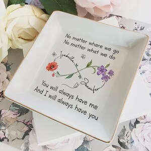 Op de afbeelding: Vierkante witte keramische sieradenschaal met gouden rand. De schaal heeft bloemen- en vlinderontwerpen, de namen "Isabella" en "Jennifer" en de tekst "No matter where we go, No matter what we do, You will always have me, And I will always have you."