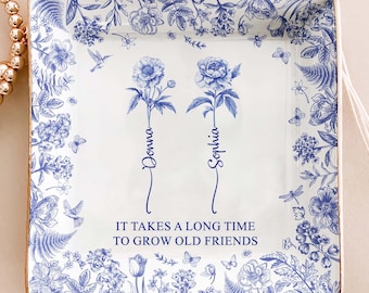 May include: Square ceramic tray with a blue and white floral design. The tray features two blue flower illustrations with the names "Donna" and "Sophia" below. The text "IT TAKES A LONG TIME TO GROW OLD FRIENDS" is also displayed.