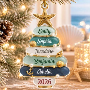 Peut inclure: Une décoration de sapin de Noël sur le thème côtier, formée d'une pile de galets lisses aux tons bleu, vert et blanc. Elle comporte une étoile de mer dorée au sommet, des fils dorés, des perles blanches, des coquillages, une ancre et les prénoms Emily, Sophia, Theodore, Benjamin, Amelia, ainsi que l'année 2026.