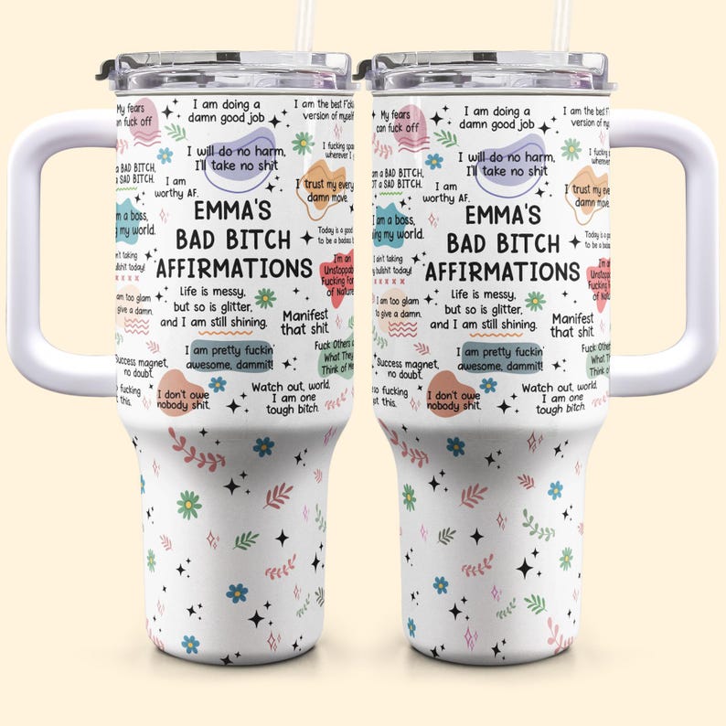 May include: Two white travel mugs with handles, featuring the text "EMMA'S BAD BITCH AFFIRMATIONS" and various affirmations. The mugs have a floral pattern with stars and colorful accents. Each mug has a white lid and a straw.