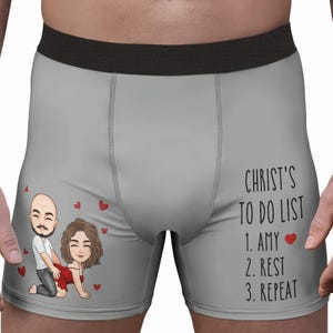 May include: Grey boxer shorts with a black waistband. The left side features a cartoon couple and red hearts. The right side has the text "CHRIST'S TO DO LIST" followed by "1. AMY", "2. REST", and "3. REPEAT".