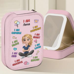May include: A pink travel makeup case with a cartoon illustration of a girl and the name "Anna". The case is decorated with positive affirmations like "I am capable" and "I am confident". An open case reveals a built-in mirror.