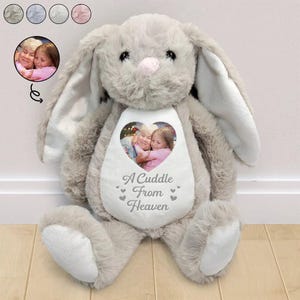 May include: A plush grey rabbit stuffed animal with long ears and a white belly patch. The belly features a heart-shaped photograph of two people and the printed text A Cuddle From Heaven, accented with small grey hearts on the white fabric.