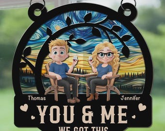 May include: A black wooden sign with a decorative border and a painting-like background. The sign features two cartoon figures seated in chairs, holding wine glasses. The text "YOU & ME WE GOT THIS" is displayed on the bottom.