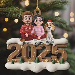 Peut inclure: Ornement de Noël représentant une famille et son chien. L'ornement affiche l'année 2025 en chiffres en bois. Les membres de la famille portent des pulls assortis, assis sur une base enneigée. Le chien porte un bonnet de Père Noël.