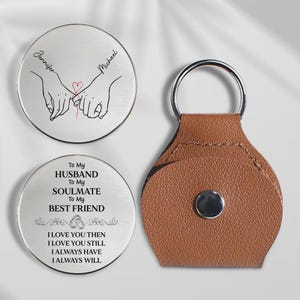 Peut inclure: Ensemble de cadeaux personnalisés, comprenant deux jetons ronds argentés et un porte-clés en cuir marron. Un jeton présente des mains jointes avec un cœur rouge et des noms. L'autre porte le texte : "To My Husband, Soulmate, Best Friend."