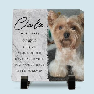 May include: A white marble memorial stone with a black paw print and wings. The stone has the text "Charlie 2018 - 2024" and "If love alone could have saved you, you would have lived forever". A photo of a small, light brown dog is on the right side of the stone.