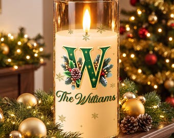 May include: A cylindrical glass candle holder containing a white wax candle with a lit flame. The candle features a large green letter W decorated with pine branches, berries, and pinecones, with the text The Williams printed below.