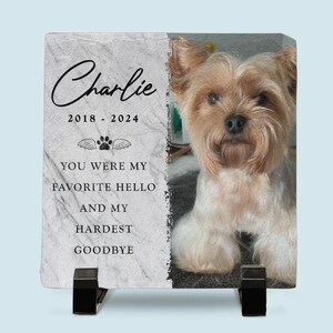 May include: A white marble memorial stone with a photo of a small, light brown dog. The text "Charlie 2018 - 2024" is printed on the stone, along with the words "You were my favorite hello and my hardest goodbye".