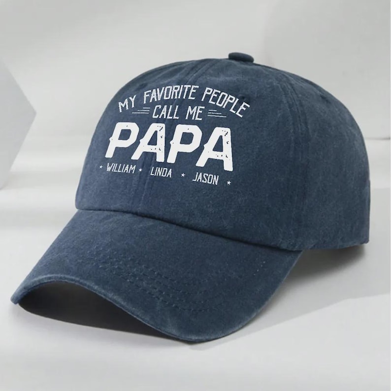 May include: A navy blue baseball cap with the text "MY FAVORITE PEOPLE CALL ME PAPA" in white. Below the word "PAPA" are the names "WILLIAM", "LINDA", and "JASON". The cap has a curved brim and a button on top.