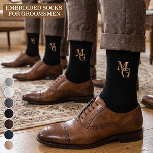 May include: Black ribbed socks featuring gold embroidered initials MG, worn with brown leather brogue dress shoes and brown trousers. The text EMBROIDERED SOCKS FOR GROOMSMEN is visible at the top, along with a color selection palette.