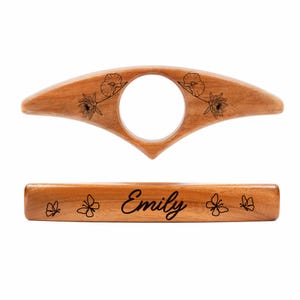 May include: A wooden book holder and page holder set. The book holder has a large center hole and floral designs. The page holder is engraved with the name "Emily" and butterfly designs. Both are made of light brown wood.