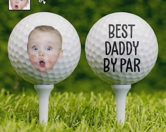 Può includere: Due palline da golf bianche su tee in erba verde. Una pallina ha stampata la faccia di un bambino. L'altra pallina ha la scritta "BEST DADDY BY PAR" stampata in nero. Una piccola immagine del bambino è nell'angolo in alto a sinistra.