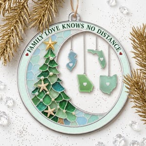May include: A circular silver-toned ornament featuring a green stained-glass style Christmas tree with starfish and pearls. The text "FAMILY LOVE KNOWS NO DISTANCE" is printed along the top. Four state-shaped charms hang from the frame.