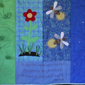 May include: A green, blue, and white patchwork quilt with a flower, fireflies, and a quote from Psalm 42:9: "By day the Lord directs His love, At night His song is with me- A prayer to the God of my life."