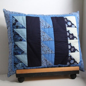 May include: A blue and white patterned cushion with a geometric design. The cushion is on a wooden stand with black wheels.