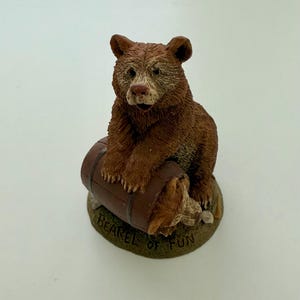 May include: A brown bear figurine sitting on a barrel with the text "Barrel of Fun" on the base.