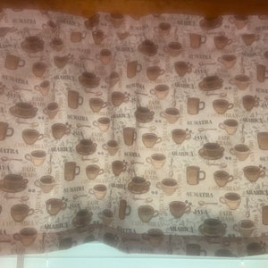 May include: A beige fabric with a repeating pattern of coffee cups, coffee beans, and the words "Sumatra", "Java", "Fair Trade", and "Arabica".