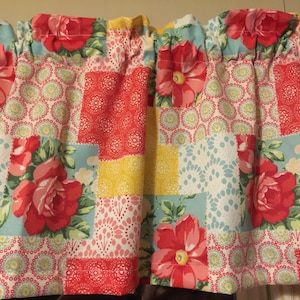 May include: A window valance featuring a patchwork design with alternating blocks of red roses on a light blue background, yellow floral patterns, and red circular geometric prints. The fabric is gathered at the top to create a ruffled header.