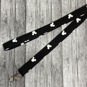 May include: Black lanyard with a white Mickey Mouse head pattern. The lanyard has a silver swivel clip.