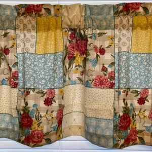 May include: A floral valance with a patchwork design. The valance features squares of beige, yellow, and light blue fabric, each with a different pattern. Some squares have floral prints, while others have polka dots or geometric designs. The valance is trimmed with a scalloped edge.