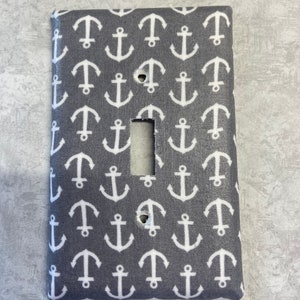 May include: A gray light switch cover with a white anchor pattern.