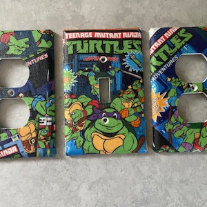 May include: Three Teenage Mutant Ninja Turtles themed light switch and outlet covers. The covers feature a comic book style design with the Teenage Mutant Ninja Turtles logo and characters. The covers are made of durable plastic and are easy to install.