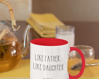 May include: White ceramic mug with a red rim and handle. The mug has black text that reads "Like Father. Like Daughter. Oh Snap." The mug is microwave safe.