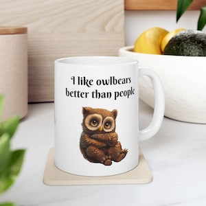 May include: White ceramic mug with a brown owlbear illustration and the text "I like owlbears better than people".
