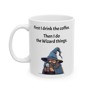 May include: White ceramic mug with a black and white illustration of a wizard drinking coffee. The mug reads "First I drink the coffee. Then I do the Wizard things."