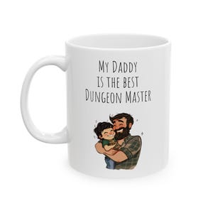 May include: White ceramic coffee mug with a black and white illustration of a father and son. The text on the mug reads "My Daddy is the Best Dungeon Master."