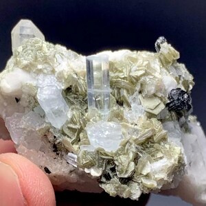 May include: A cluster of clear aquamarine crystals on a matrix of white and green feldspar. The crystals are sharp and well-formed, with a glassy lustre.