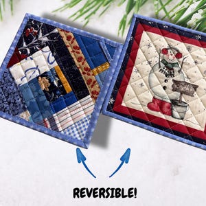 May include: Reversible quilted square coasters. One side features a patchwork design in shades of blue, red, and cream. The other side has a snowman with a sign that reads "Snowflake Sale". The coasters have a blue border.