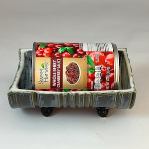 May include: A ceramic dish with a can of Sweet Harvest Whole Berry Cranberry Sauce. The can is 14 oz (397g). The dish is gray with a blue-green trim and black feet.