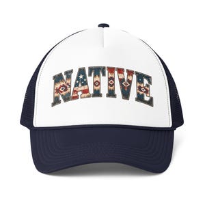 May include: A navy blue and white trucker cap featuring a white front panel with the word NATIVE printed in a distressed, multi-coloured pattern that incorporates red, white, and blue geometric shapes and stars reminiscent of the American flag.
