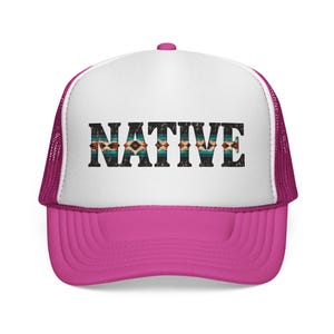 May include: A bright pink trucker cap with a white front panel. The word NATIVE is printed in large, bold, black letters across the centre, featuring a distressed texture and a colourful geometric pattern inside the lettering.