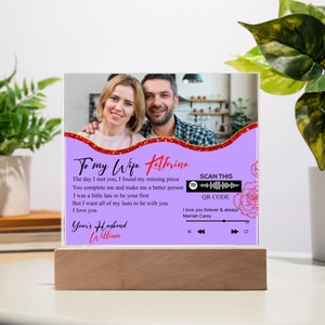 May include: A purple and white personalized acrylic plaque with a photo of a couple. The plaque has a red and gold glitter border and a red heart with the text "To my Wife Katrina". The text "The day I met you, I found my missing piece. You complete me and make me a better person. I was a little late to be your first. But I want all of my lasts to be with you. I love you. Your's Husband William" is printed on the plaque. A Spotify logo and a QR code are also included on the plaque.