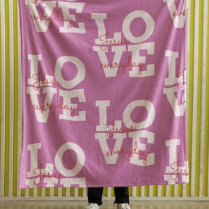 May include: A pink fleece blanket with the word "LOVE" repeated in white letters. The words "Jesus" and "everyday" are written in red cursive script within the letters.