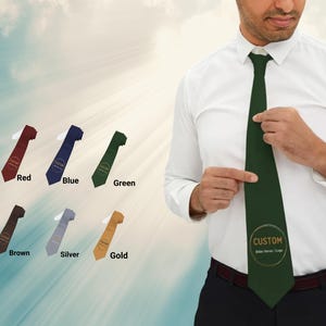 Puede incluir: Una selección de corbatas en varios colores, incluyendo rojo, azul, verde, marrón, plateado y dorado. Un hombre lleva una corbata verde con un logotipo personalizado. Las corbatas se muestran sobre un fondo suave y claro.