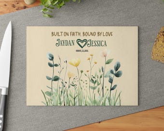 May include: A rectangular cutting board with a floral design and the text "BUILT ON FAITH, BOUND BY LOVE" above the names "JAYDAN" and "JESSICA" with a heart symbol. The date "AUGUST, 23, 2025" is below the names.