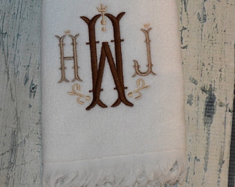 May include: White hand towel with a brown embroidered monogram of the letters "AWJ" with decorative flourishes.