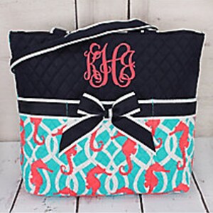 May include: A navy blue tote bag with a white trim and a large black bow. The bag has a turquoise and white pattern with pink seahorses. The bag is monogrammed with the initials "K.H.B."