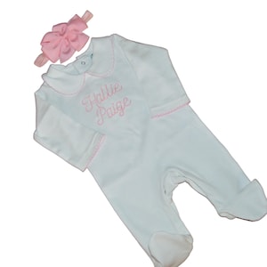 May include: White baby onesie with a pink bow headband. The onesie has a pink embroidered collar and the name "Hallie Paige" embroidered on the front.