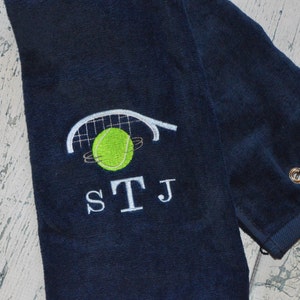 May include: A dark blue towel with a white tennis racket and ball design. The towel has a loop for hanging and the initials STJ embroidered in white.